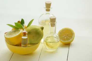 Cytryny i połówka cytryny w misce z liśćmi, obok szklane butelki z żółtym olejkiem