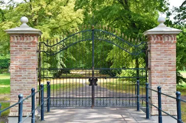 Czarna metalowa brama między ceglanymi filarami w parku