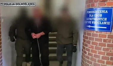 Funkcjonariusze prowadzą zatrzymanego w kajdankach do pomieszczeń dla zatrzymanych KMP we Wrocławiu.