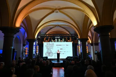 Wnętrze sali z gotyckimi sklepieniami, gdzie mówca stoi przy pulpicie przed ekranem z napisem „II Forum Mecenatu Kultury” podczas konferencji z udziałem publicz