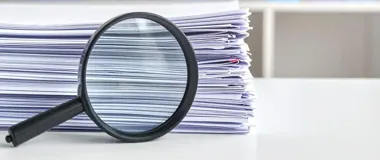 Lupa opiera się o grubą stertę dokumentów ułożonych na białym biurku.