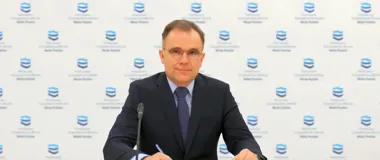 Mężczyzna w garniturze i krawacie siedzi przy stole z mikrofonem podczas konferencji prasowej przed ścianką z logo Państwowego Gospodarstwa Wodnego Wody Polskie